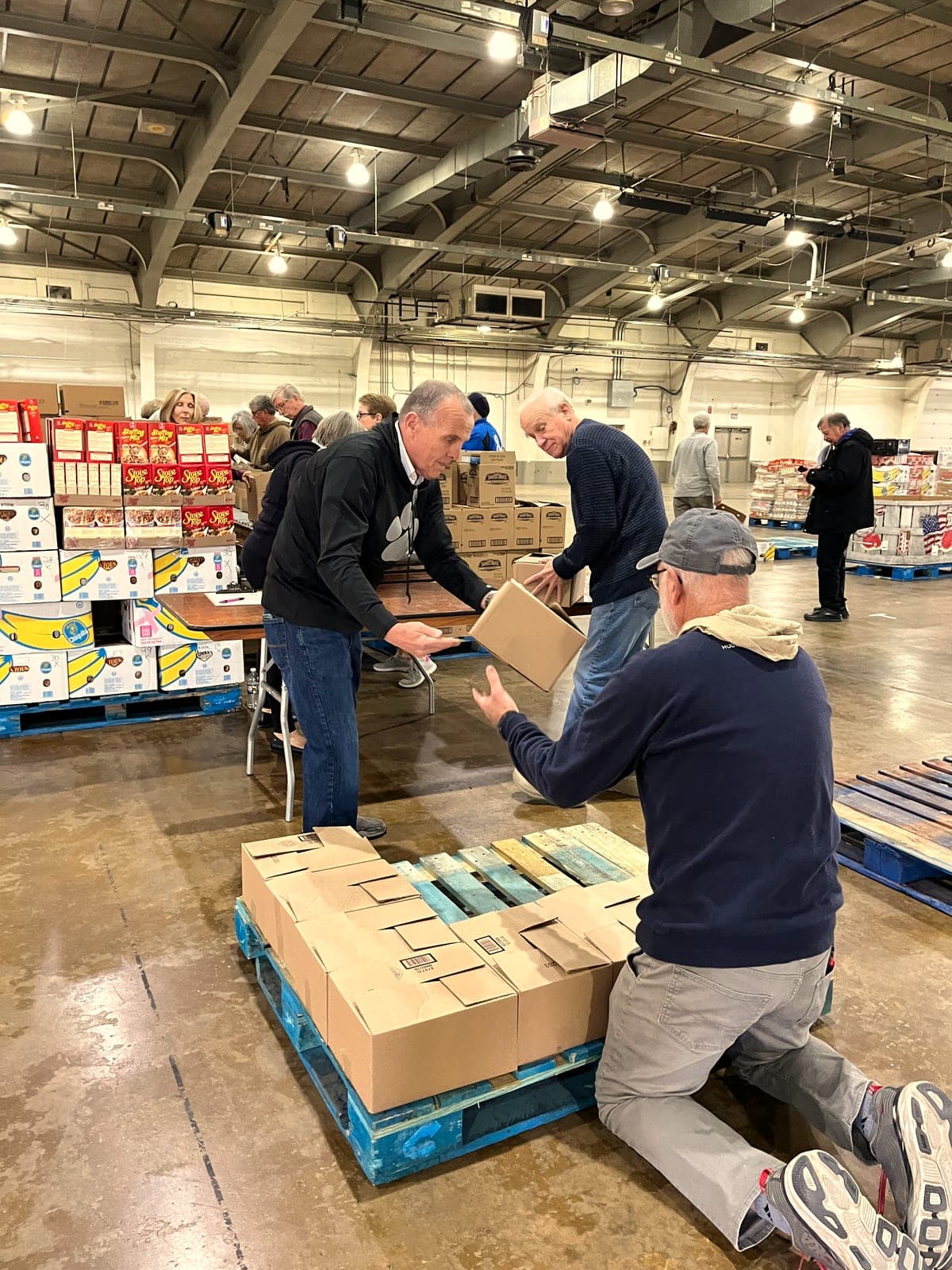 Three volunteers loading pallets of boxes in a warehouse.