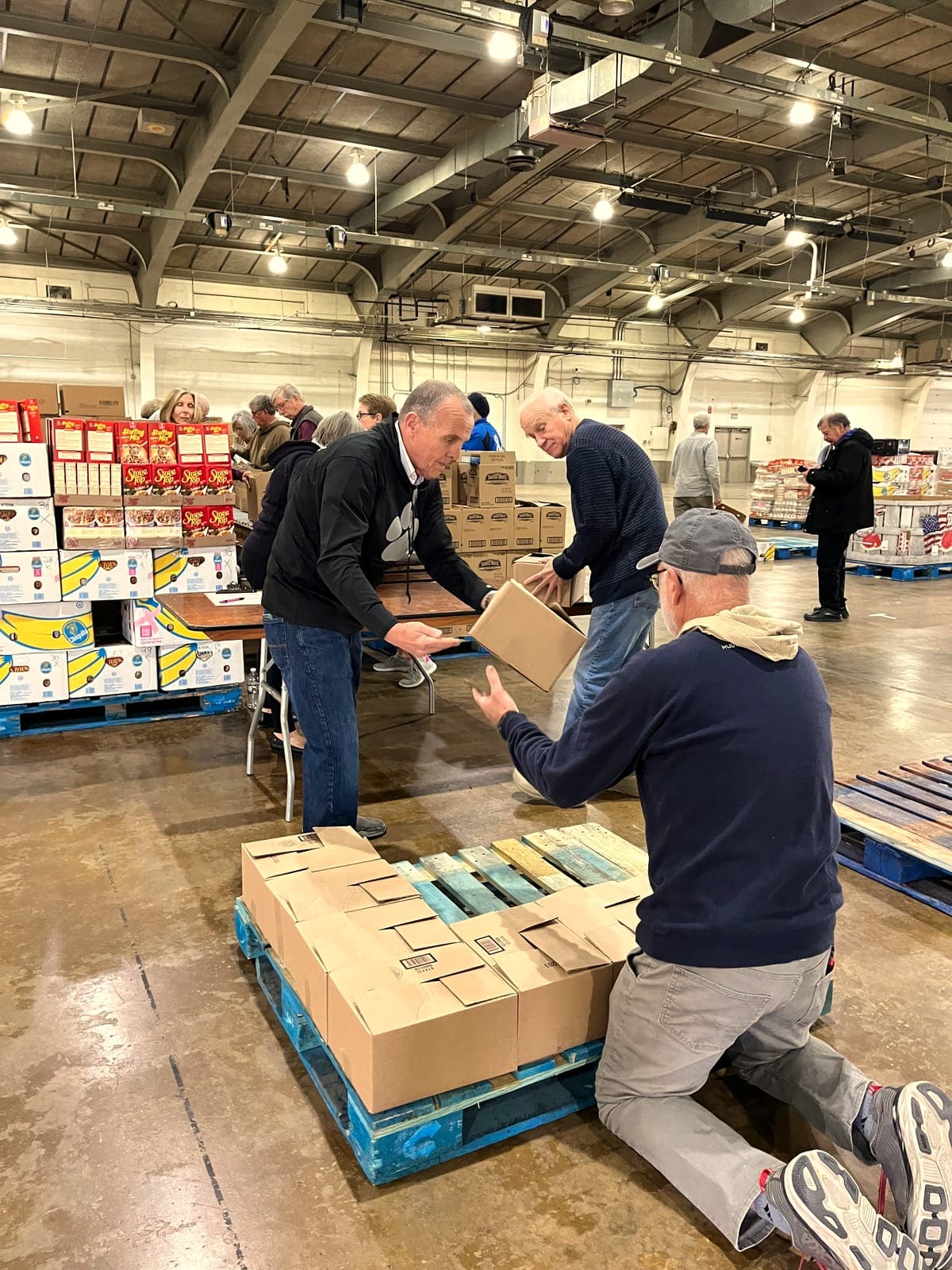 Voluntarios cargando tarimas de cajas en un almacén.